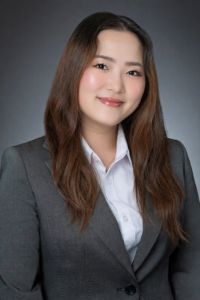 A woman in a business suit smiles in a professional studio headshot against a gray background.