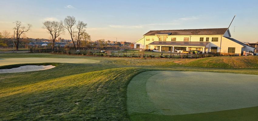 A wide view of a golf course and clubhouse at sunset with manicured greens and surrounding trees.
