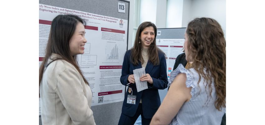 Students stand and talk together in front of research posters during an academic poster presentation session.
