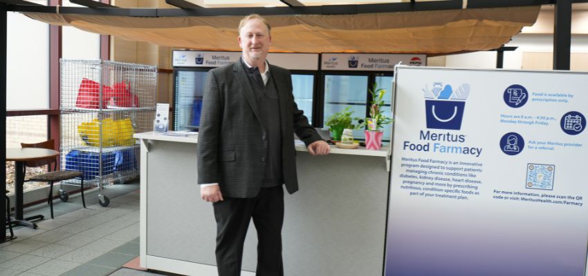 A man stands beside a sign for a food pharmacy program inside a healthcare facility.