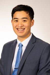 A man in a suit smiles in a professional headshot against a neutral background.