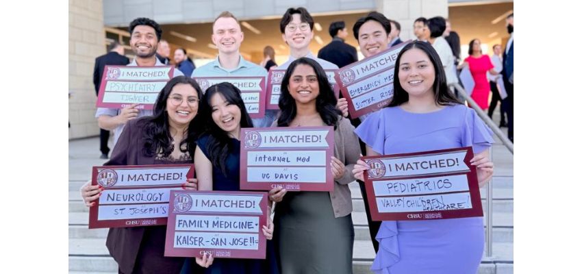 A group of medical students stand on steps smiling and holding “I Matched” signs showing their residency placements.