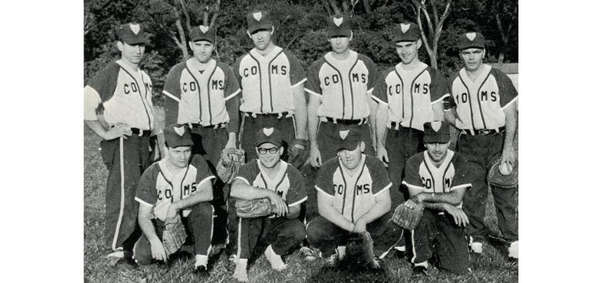 A black-and-white photo shows a vintage baseball team posing together in uniforms on a field.