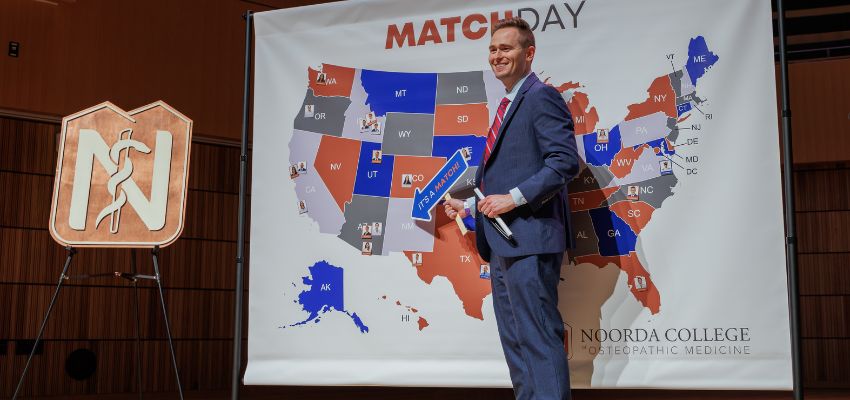 A man stands on stage in front of a U.S. map display during a Match Day event presentation.