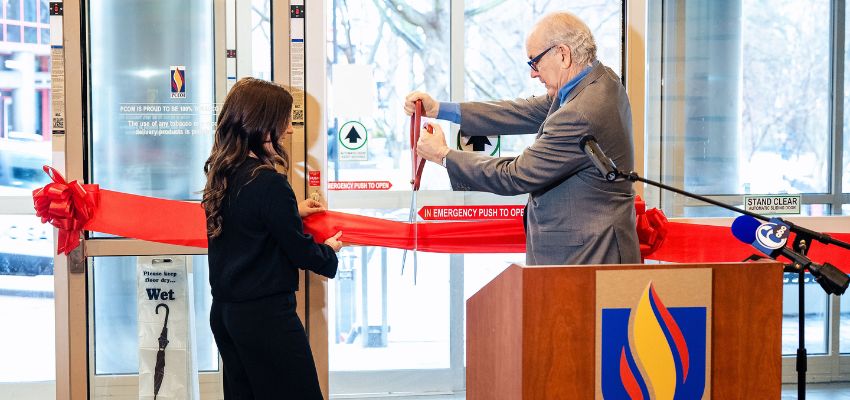 A ribbon-cutting ceremony takes place as a man cuts a red ribbon while another person holds it steady.