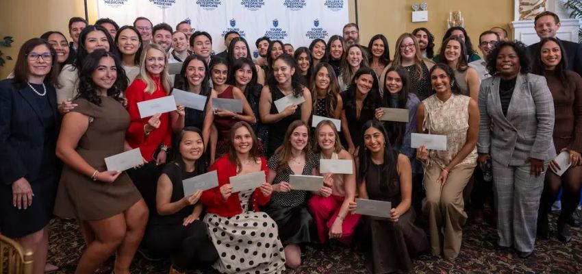 A large group of students pose together indoors holding envelopes during a celebratory event.