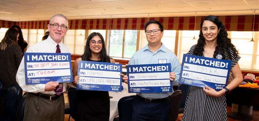 Four individuals stand indoors holding “I Matched” signs announcing their residency placements.