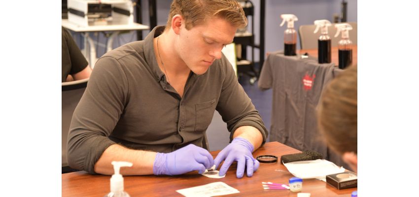 A student wearing gloves performs a hands-on lab activity while working at a table with supplies.