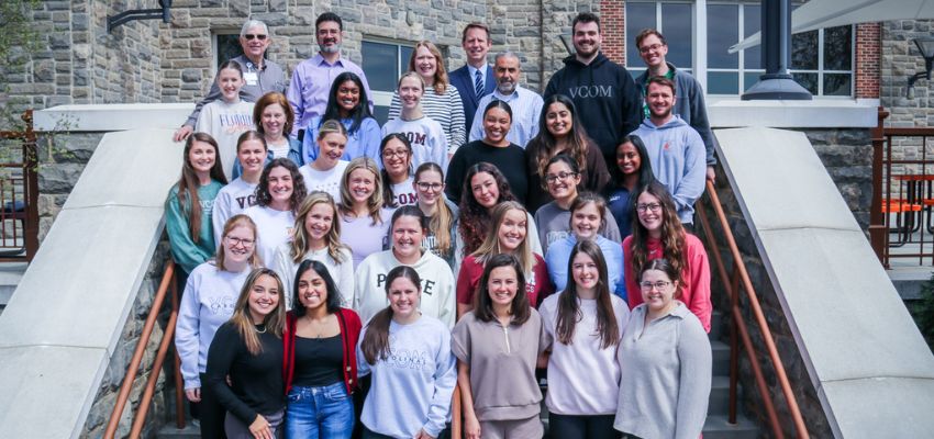 A large group of students and faculty pose together outdoors on steps in front of a building.