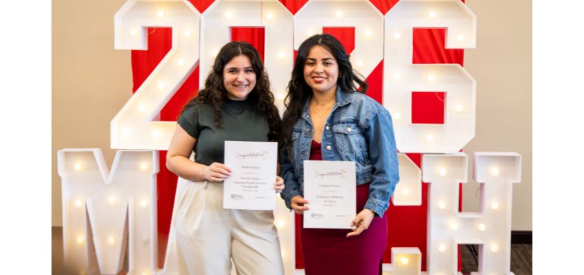 Two students stand smiling and holding certificates in front of a large “2026 MATCH” display.