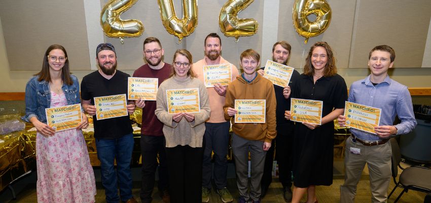 A group of students stand together holding “I Matched” signs beneath gold balloons spelling “2026.”
