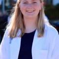 Amedicalstudentinawhitecoatsmilesinaprofessionaloutdoorheadshot
