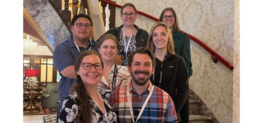 A group of colleagues pose together smiling on a staircase inside a building.