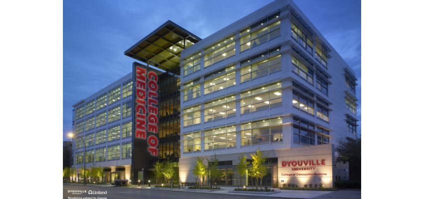 Exterior view of a modern academic building labeled “College of Medicine” at dusk with lights on inside.