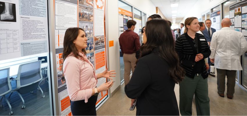 Attendees discuss research posters displayed along a hallway during a medical research event.