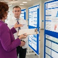 Apresenterreviewsaresearchposterwithanattendeewhileholdingaclipboardataconference