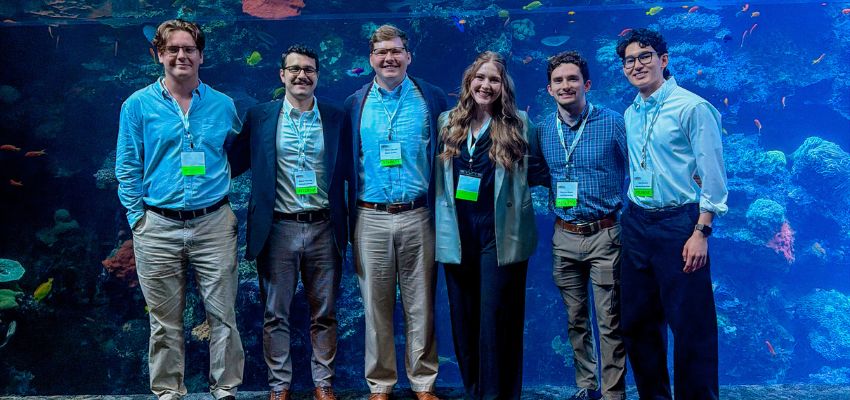 A group of people wearing name badges stand together in front of a large aquarium filled with fish.