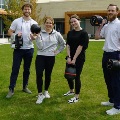 Fourpeoplestandonalawnoutsideacampusbuildingholdingdumbbellsandamedicineballsmilingatthecamera