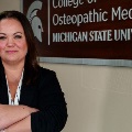 AwomanstandswitharmscrossedinfrontofawallsignreadingCollegeofOsteopathicMedicineMichiganStateUniversity