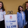 ThreepeoplestandbesideasignthatreadsWelcometoVCOMinanofficeorlobbyarea