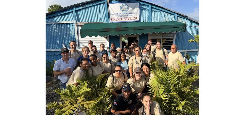 Students and volunteers take a group photo among the ferns in front of a church.