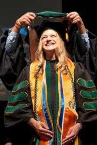 Chloe Kilkuts stands smiling while receiving her doctoral cloak.
