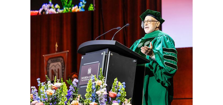 A speaker in green academic regalia delivers remarks at a podium during a Noorda College of Osteopathic Medicine ceremony.