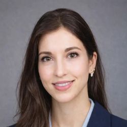 Professional headshot of a woman in business attire smiling against a neutral gray background.