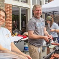 Twopeoplegrillfoodoutdoorswhileothersassistatacommunitycookoutevent