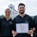 FourVCOMSportsMedicinestudentsposetogetheroutdoorswithonestudentholdingacertificate