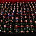 Alargegroupofgraduatesinacademicregaliaposestogetherinanarenawithredstadiumseatinginthebackground