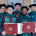 Fivegraduatesinacademicregaliasmileandholddiplomacoversoutdoorsfollowingagraduationceremony