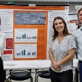 Threestudentsstandinfrontofaresearchposterandsmileduringaresearchsymposiumorpostersession