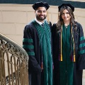 Twograduatesinacademicregaliaposetogetherbesideadecorativestaircaseinsideahistoricbuilding