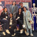 Agroupofstudentsposesonastagedecoratedwithscience-themedpropsincludingaskeletonmodelduringastudenteventorcompetition