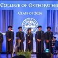 StudentleadersinacademicregaliastandonstageduringaChicagoCollegeofOsteopathicMedicineClassof2026whitecoatormilestoneceremony