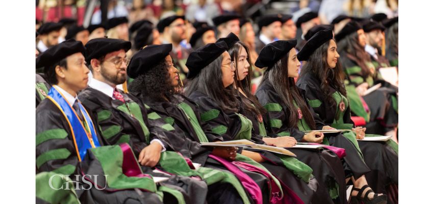Medical students seated in academic regalia listen attentively during a commencement ceremony.
