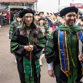 Graduatesinacademicregaliawalkthroughaprocessionlinewhilefacultyandguestsapplaudduringacommencementcelebration