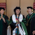 Agraduatewearinghonorcordsandaceremonialstolesmilesduringagraduationrecognitioneventalongsideuniversityleadersandfacultymembers