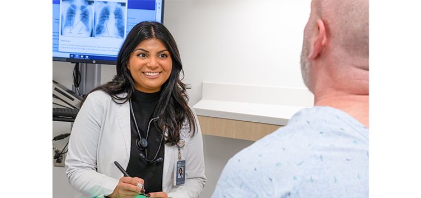 A student physician speaks with a patient during a clinical appointment in an examination room.