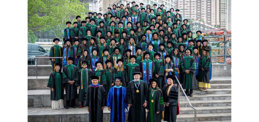 Graduating osteopathic medical students and faculty pose for a class photo on outdoor steps in front of an urban campus building.