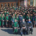 Membersofthegraduatingclassandfacultygatheroutsideatheaterforaformalclassphotoinacademicregalia