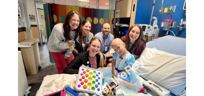 Medical students and healthcare staff gather around a pediatric patient in a hospital room, smiling together during a visit.