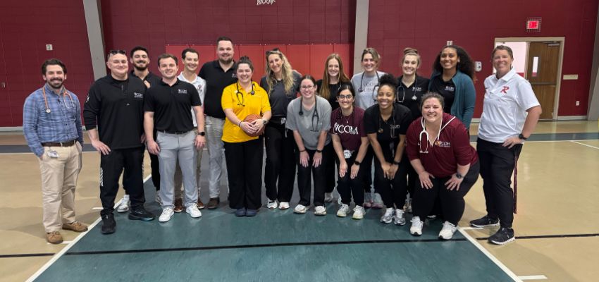 A group of medical students, faculty, and staff pose together in a gymnasium during a community or campus wellness event.