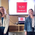 FourstudentsstandtogetherbesideapresentationscreendisplayingSisterSpeakWorkshopduringastudent-lededucationalprogram