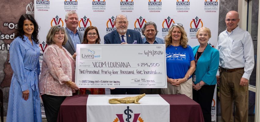 Community and institutional leaders pose with a ceremonial check recognizing funding support for VCOM-Louisiana during a presentation event.