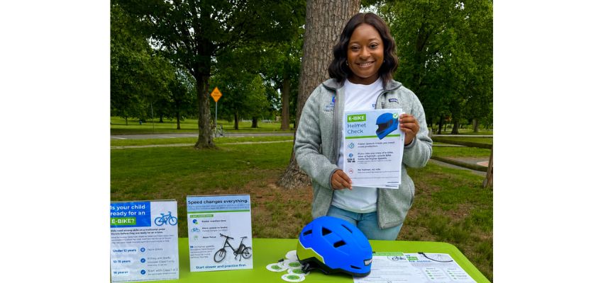 A community health educator displays e-bike safety and helmet information during an outdoor public safety event.