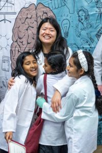 A physician embraces three young children wearing white coats during a community outreach event.
