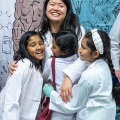 Aphysicianembracesthreeyoungchildrenwearingwhitecoatsduringacommunityoutreachevent