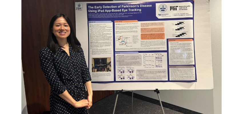 A medical student stands beside a research poster on the early detection of Parkinson's disease using iPad-based eye tracking during a scientific conference.